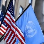 "American flag and United Nations flag waving side by side in front of a government building, symbolizing international cooperation."